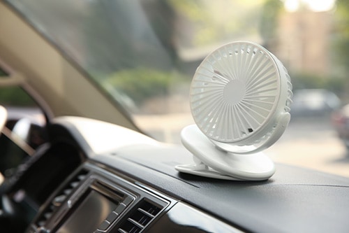 How to Keep Your Vehicle Cool in Hot Months | Iowa City Tire & Auto Image inside the hot summer using the car AC and a little fan to keep it the cool in summer