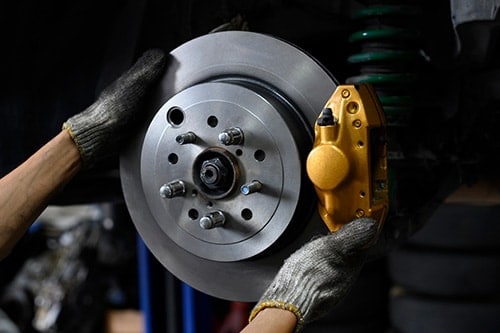 Auto mechanic installing two piston brake calipers and disc brake rotor | Iowa City Tire and Services