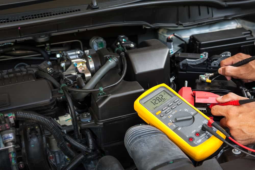 Car battery testing in Iowa City, IA with Iowa City Tire and Service. Image of mechanic testing car battery with multimeter in shop.